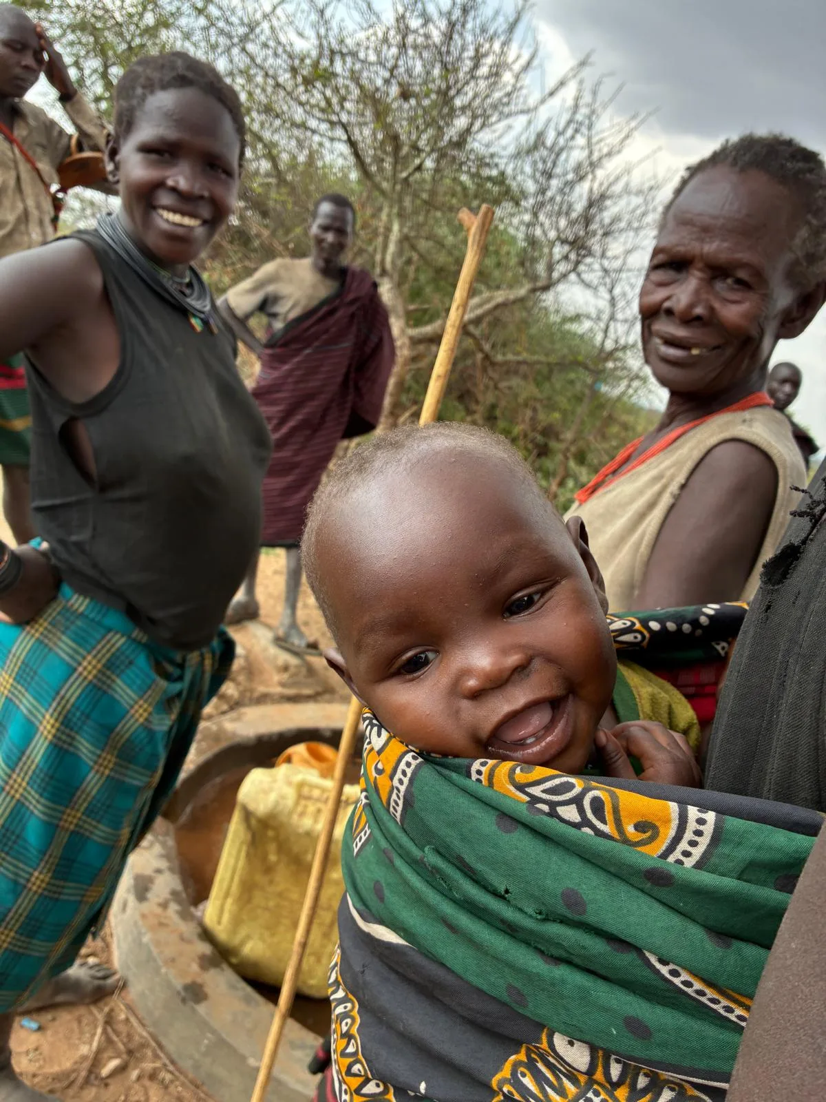 Villagers gathered at a well, a baby smiling at the camera